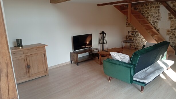 A living room with a television, wooden furniture, a green sofa, and a staircase.
