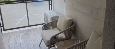 A balcony with two wicker chairs and a small table, a view of the street, and a building with a satellite dish.