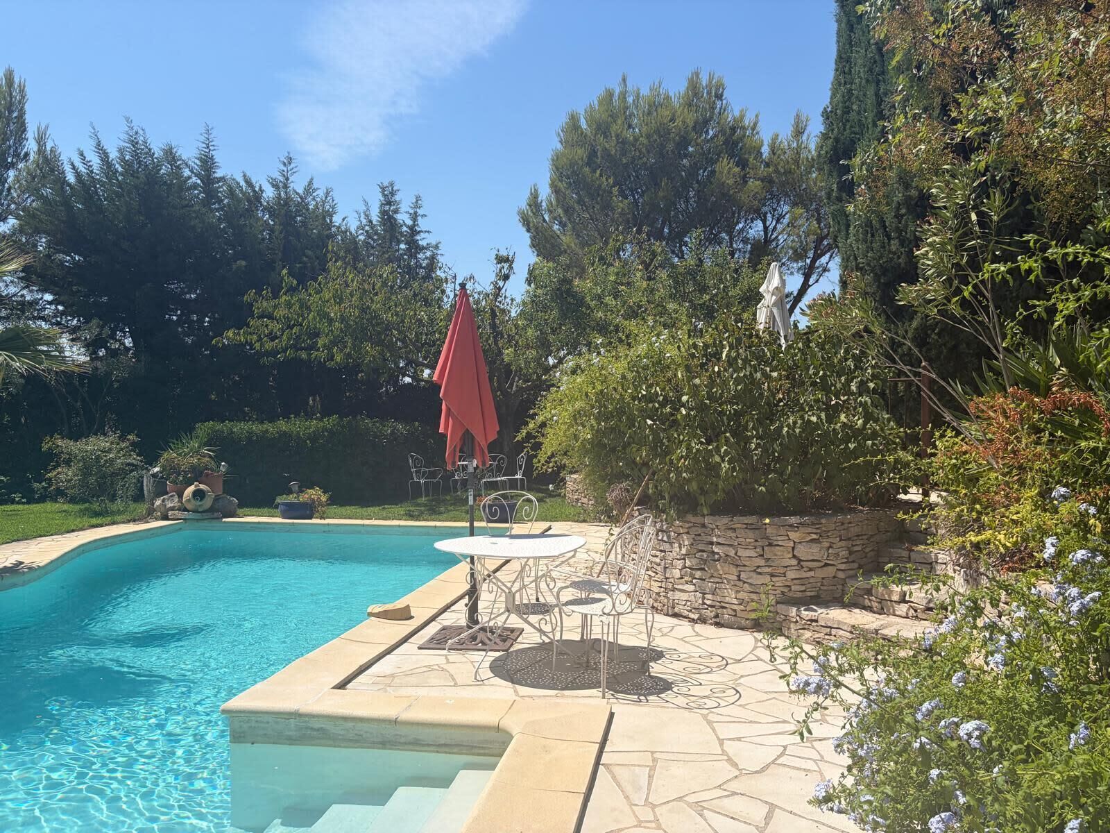 A swimming pool with a stone deck, surrounded by trees and a stone wall.