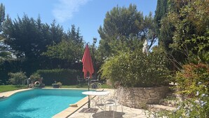 Una piscina con bordo in pietra, circondata da alberi e un muro in pietra.