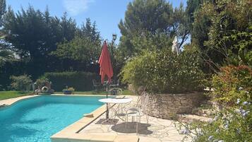 A swimming pool with a stone deck, surrounded by trees and a stone wall.