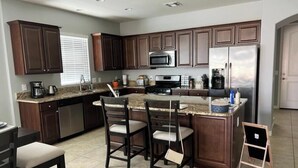 A modern kitchen with dark wood cabinets, a stainless steel refrigerator, a microwave, and a granite countertop. - Beautiful desert rancher with heated pool and spa, surrounded with palm trees (Maricopa)