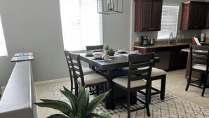 A dining area with a table and chairs, a potted plant, and a kitchen in the background. - Beautiful desert rancher with heated pool and spa, surrounded with palm trees (Maricopa)