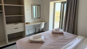 A hotel room with a bed, a desk, a chair, a wardrobe, and a window with curtains. - Sunrise Village Aptera Private Pool Villa I (Souda)