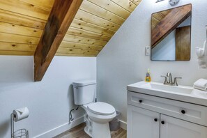 A bathroom with a wooden ceiling, a white toilet, a sink with a mirror, and a bottle of hand soap. - Classic Tahoe Cabin Near Beaches, Mountain Bike Trails & Year-Round Adventure (South Lake Tahoe)