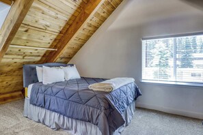 Ein Schlafzimmer mit schrägemaßter Decke, einem Bett mit gesteppter blauer Bettdecke, weißen Kissen und einem gefalteten Handtuch.