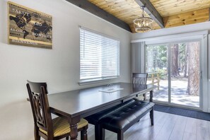 Ein Essbereich mit Holztisch, einer Bank und Stühlen, einem Fenster mit Jalousien und Blick ins Freie.