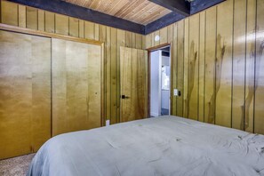 A room with wooden panel walls, a bed with a white bedspread, and a door leading to another room. - Classic Tahoe Cabin Near Beaches, Mountain Bike Trails & Year-Round Adventure (South Lake Tahoe)