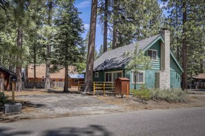 A cabin with a wooden deck, surrounded by tall pine trees.