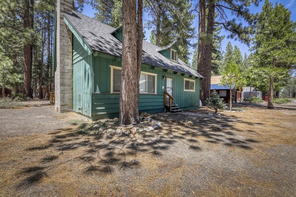 A small, single-story cabin with a green exterior, surrounded by pine trees. - Classic Tahoe Cabin Near Beaches, Mountain Bike Trails & Year-Round Adventure (South Lake Tahoe)