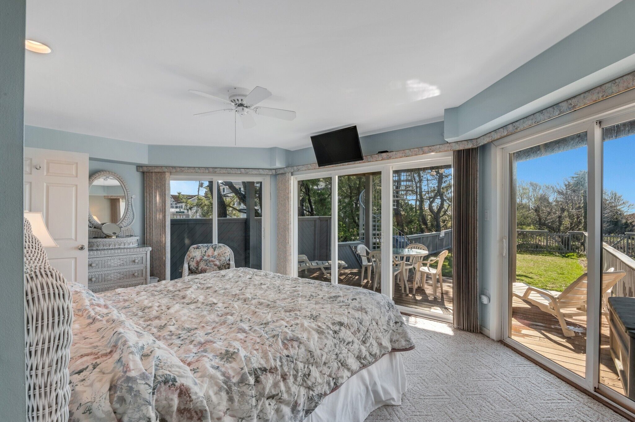 Un dormitorio con una cama grande, un ventilador de techo y un ventanal corredero que da a un patio exterior.