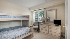 Ein Schlafzimmer mit Etagenbett, Schreibtisch mit Stuhl, Kommode, Fernseher und Fenster mit Jalousien.