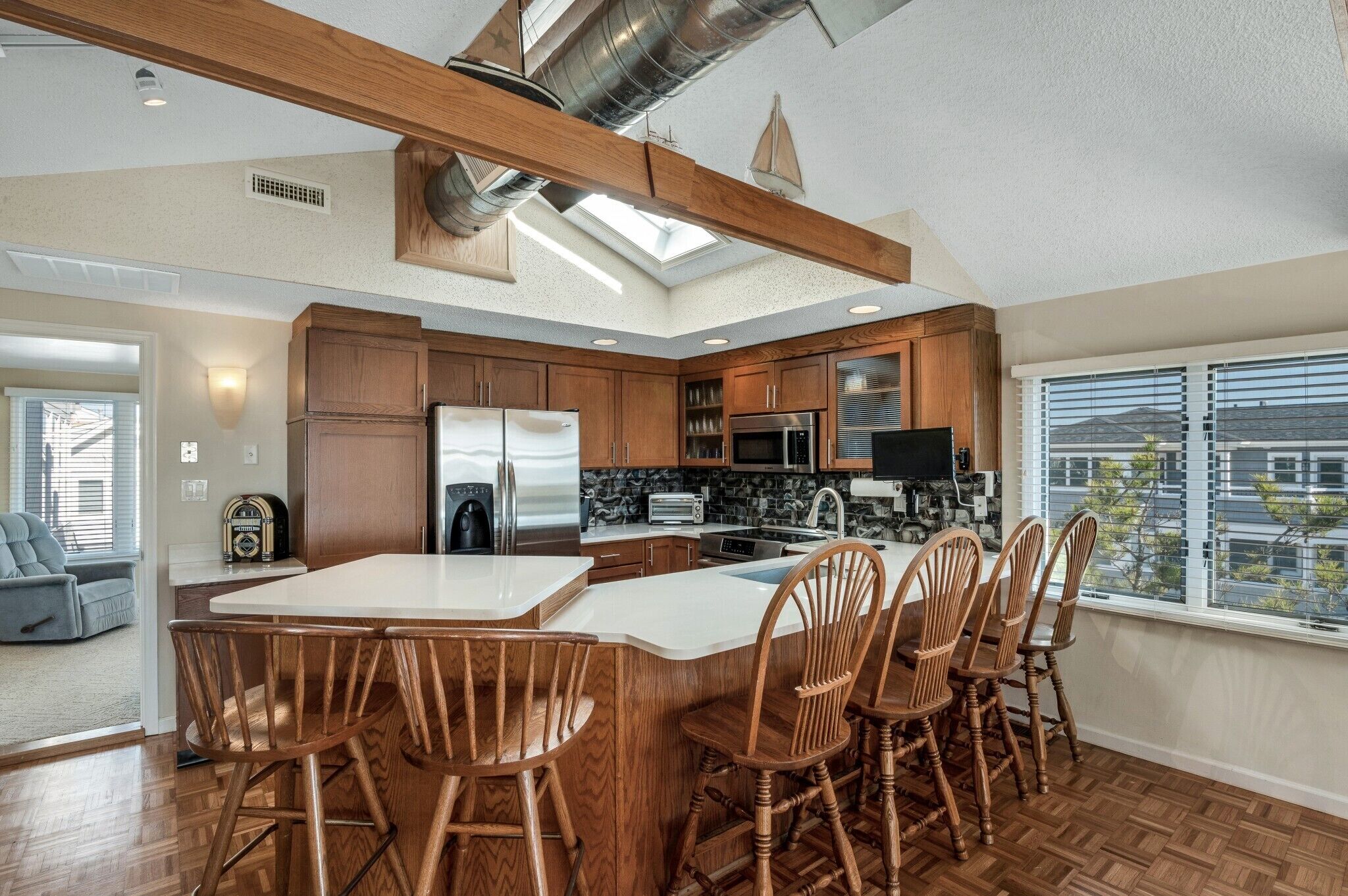 Une cuisine moderne avec un îlot central, des chaises en bois et une vue sur l’extérieur.