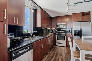 A modern kitchen with stainless steel appliances, wooden cabinets, and a large window. - Pelican Cove 505 - A Quiet Getaway Awaits (Indian Rocks Beach)