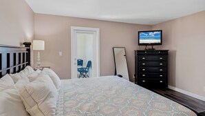 A bedroom with a bed, a dresser, a television, and a door. - Pelican Cove 505 - A Quiet Getaway Awaits (Indian Rocks Beach)