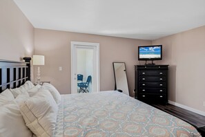 A bedroom with a bed, a dresser, a television, and a door. - Pelican Cove 505 - A Quiet Getaway Awaits (Indian Rocks Beach)
