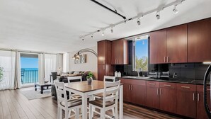 A modern kitchen with wooden cabinets and a dining area with white chairs. - Pelican Cove 505 - A Quiet Getaway Awaits (Indian Rocks Beach)