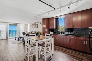 A modern kitchen with wooden cabinets and a dining area with white chairs. - Pelican Cove 505 - A Quiet Getaway Awaits (Indian Rocks Beach)
