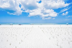 A beach with white sand, clear blue sky, and a few people and umbrellas. - Pelican Cove 505 - A Quiet Getaway Awaits (Indian Rocks Beach)