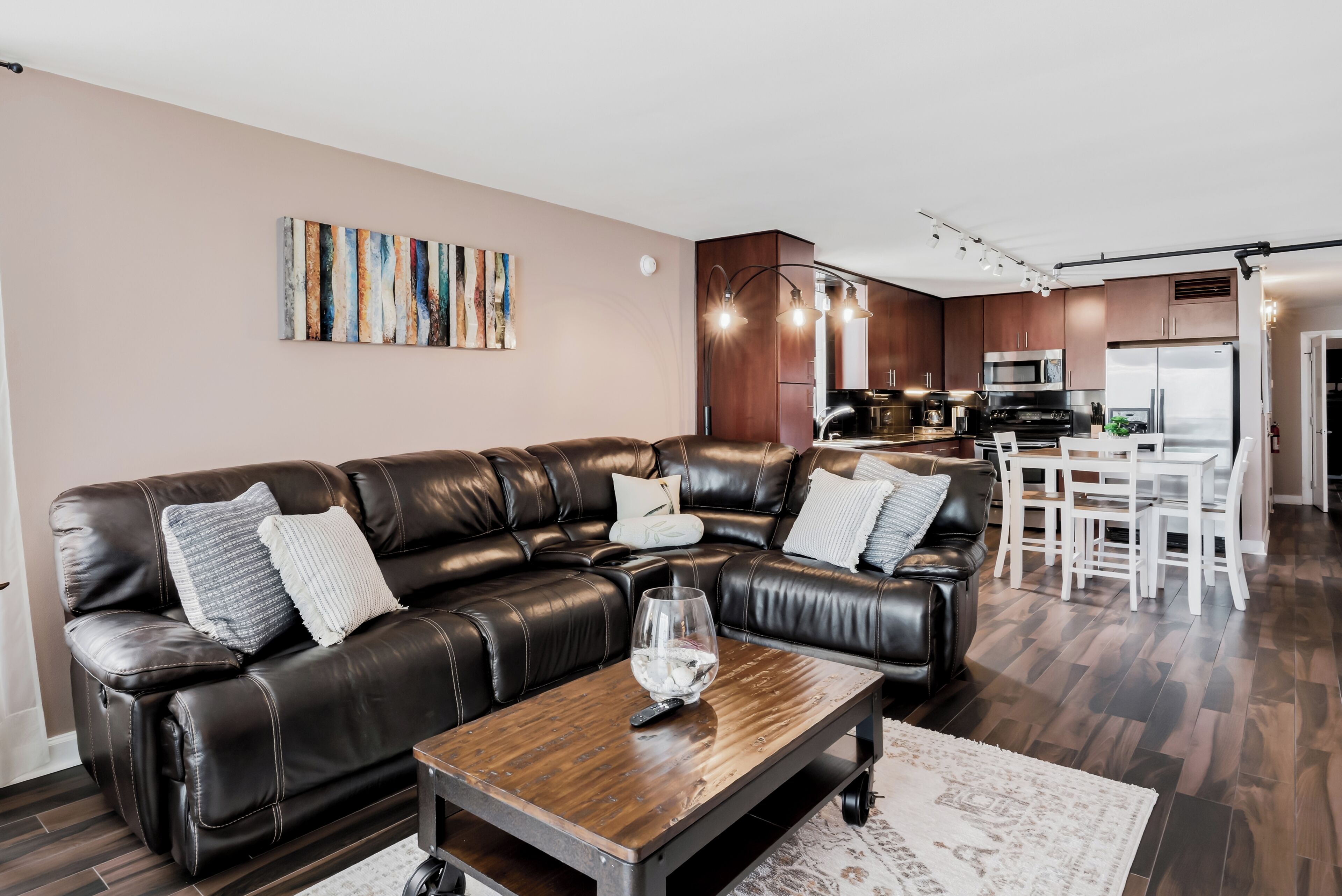 A modern living room with a leather sofa, a wooden coffee table, and a kitchen in the background.