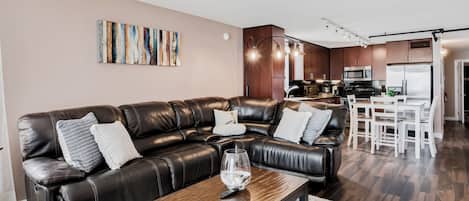 A modern living room with a leather sofa, a wooden coffee table, and a kitchen in the background.