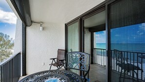 A balcony with a round table and two chairs, a sliding glass door, and a view of the ocean. - Pelican Cove 505 - A Quiet Getaway Awaits (Indian Rocks Beach)