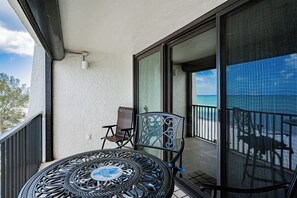 A balcony with a round table and two chairs, a sliding glass door, and a view of the ocean. - Pelican Cove 505 - A Quiet Getaway Awaits (Indian Rocks Beach)