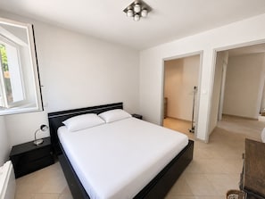 A bedroom with a bed, a nightstand, a lamp, and a window. - Roussillon : pool and tennis court (Roussillon)