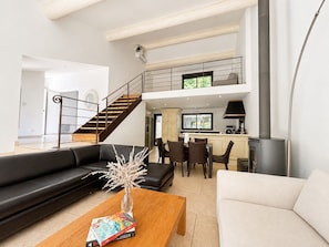 Ein modernes Wohnzimmer mit einer schwarzen Couch, einer weißen Couch, einem Holztisch und einer Vase mit Blumen. Eine Treppe führt zu einer oberen Ebene.