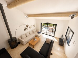 A modern living room with a sofa, a coffee table, a fireplace, and a large sliding glass door leading to an outdoor patio. - Roussillon : pool and tennis court (Roussillon)