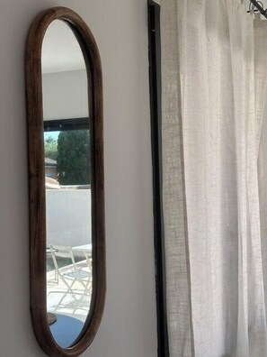 Una habitación con un espejo de marco de madera y una cortina blanca.