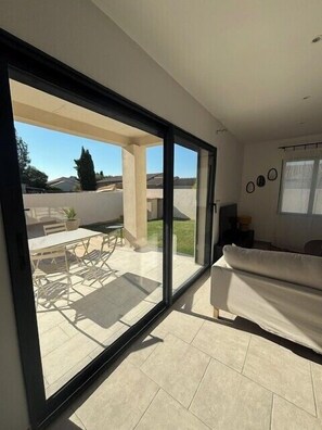 Una sala de estar moderna con un gran ventanal corredera que da a un patio al aire libre.