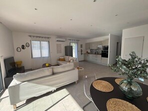 Una sala de estar moderna con un sofá, una mesa de comedor con individuales y una cocina al fondo.