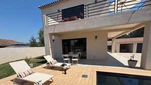 Uma casa de dois andares com piscina, móveis de exterior e um espaço de pátio coberto.