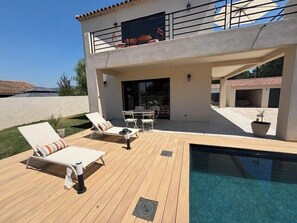 Ein zweistöckiges Haus mit Schwimmbad, Gartenmöbeln und einer überdachten Terrasse.