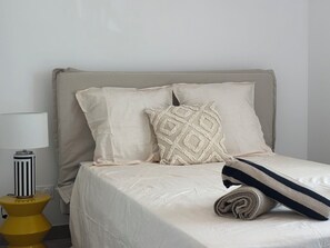 A bed with a beige headboard, two pillows, a rolled blanket, and a striped pillow. There is a lamp on a yellow base beside the bed. - Villa South Side - private pool (L'Isle-sur-la-Sorgue)