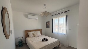 Quarto com cama, ventilador de teto, ar condicionado, janela com cortinas e tapete.