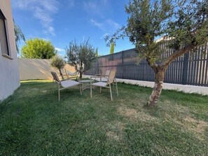 Un jardin avec une petite table et deux chaises, un arbre et une clôture.