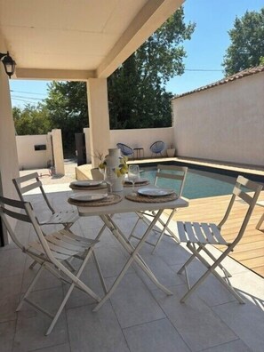 A covered outdoor area with a pool, white folding chairs, and a table set for dining. - Villa South Side - private pool (L'Isle-sur-la-Sorgue)