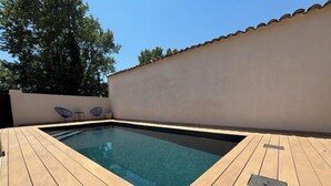 Piscina retangular com deck de madeira, cercada por um muro baixo e céu claro.