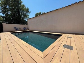 Ein rechteckiger Pool mit Holzterrasse, umgeben von einer niedrigen Mauer und blauem Himmel.
