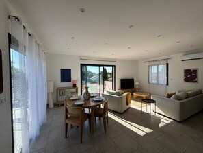 A modern living room with a dining area, a sofa, a TV, and a balcony with outdoor furniture. - Solea - Terrace Side (L'Isle-sur-la-Sorgue)