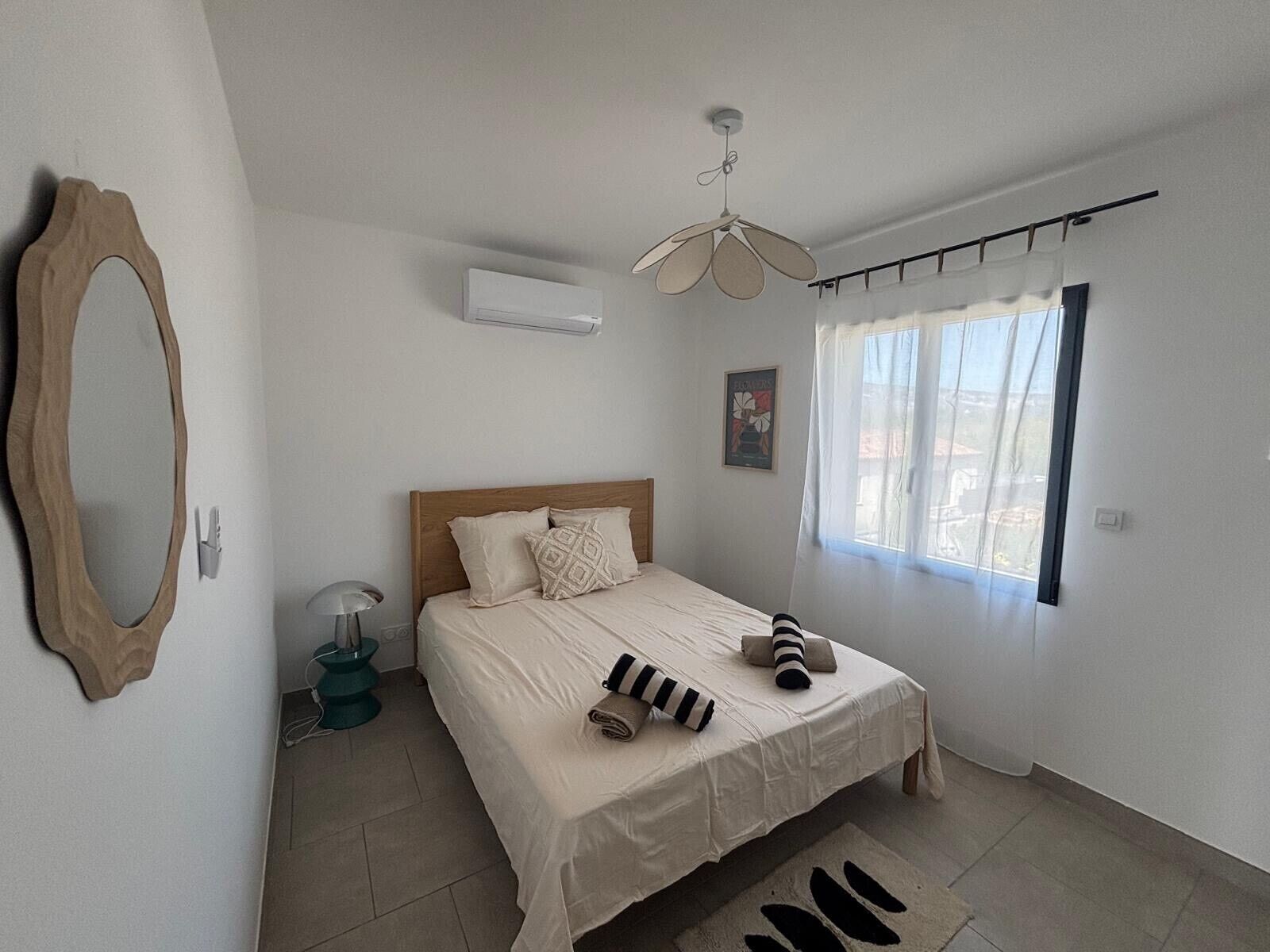 A bedroom with a bed, a ceiling fan, a window with curtains, a wall-mounted air conditioner, and a mirror.