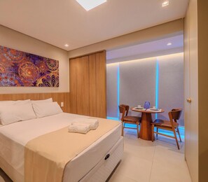 Ein Hotelzimmer mit Bett, Tisch mit Stühlen, einem Bild an der Wand und einem Fenster mit Blick.