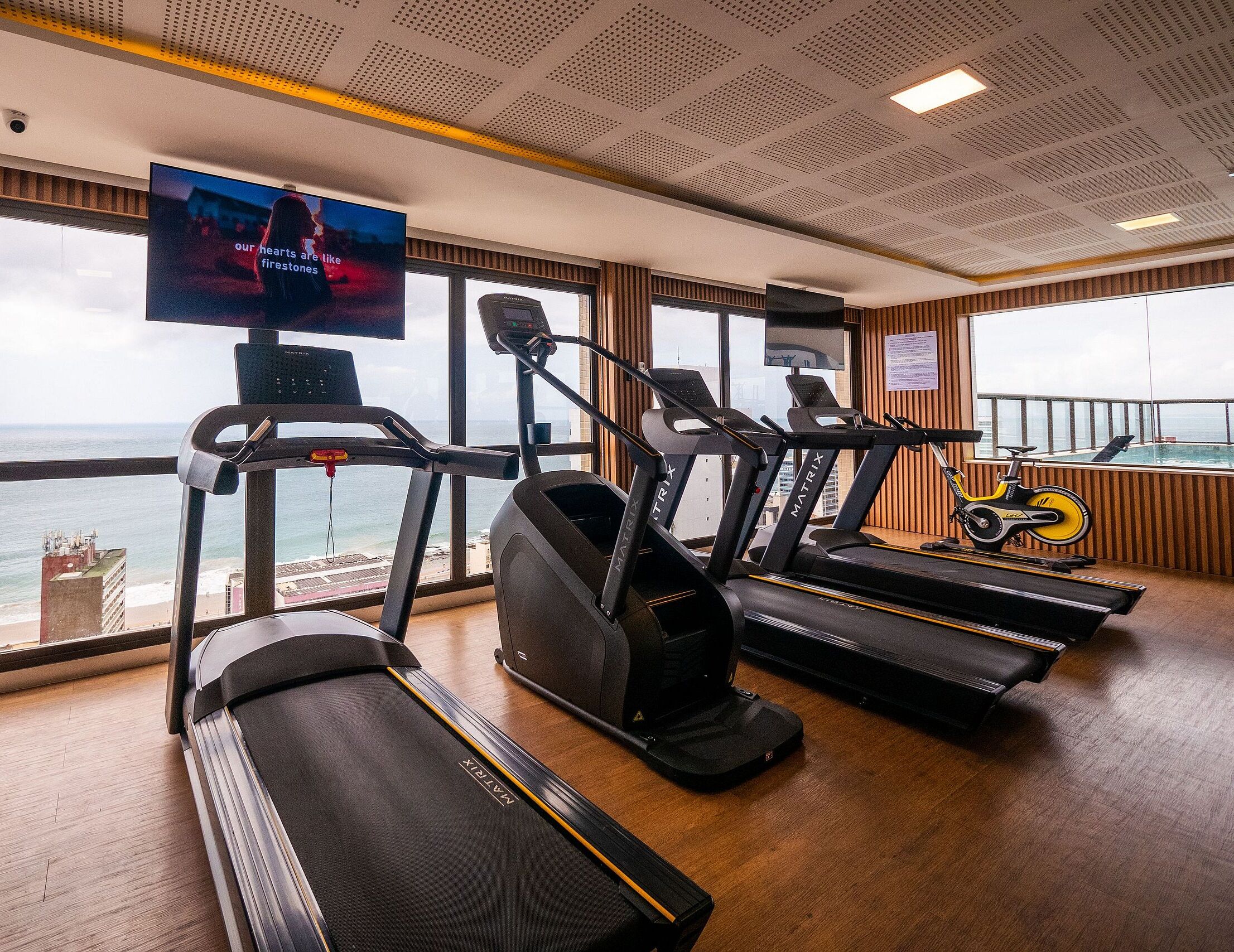 A gym with treadmills, a stationary bike, and a TV screen displaying a movie.