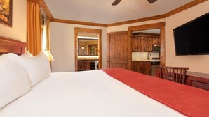 Een hotelkamer met een bed, een plafondventilator, een televisie en een keukenruimte zichtbaar door een geopende deur.