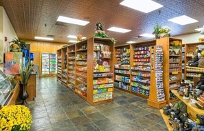 Interior de una tienda con estantes llenos de productos variados, un expositor refrigerado y una sección de zapatos.