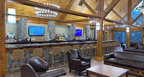 Una zona de bar con pared de piedra, varios taburetes y una pantalla de televisión.