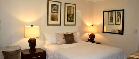 Habitación de hotel con cama, dos lámparas de noche, ventilador de techo y cuadros en las paredes.
