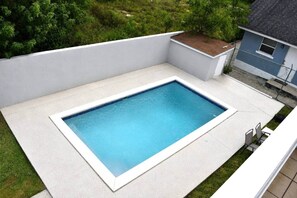 A rectangular swimming pool with a white border, surrounded by a concrete deck and a low white wall. - Tangerine Sunsets Medina (Nassau)